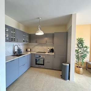Een moderne keuken met grijze kastjes, een inbouwoven, een spoelbak en een prullenbak.