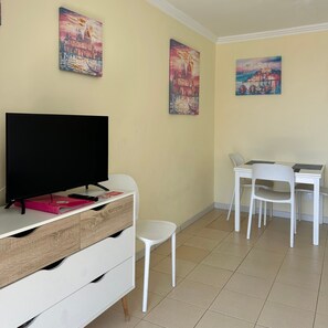 A room with a television on a wooden cabinet, a white desk with a chair, and three paintings on the wall. - Vacation Home '1 Bedroom Apartment Green Park K001' with Shared Pool and Balcony (Santa Cruz de Tenerife)