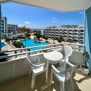 A balcony with a view of a swimming pool, white plastic chairs, and a small table. - Vacation Home '1 Bedroom Apartment Green Park K001' with Shared Pool and Balcony (Santa Cruz de Tenerife)
