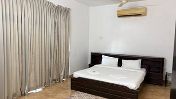 A bedroom with a bed, curtains, a ceiling fan, an air conditioning unit, and a rug.