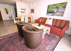 Ein Wohnzimmer mit einem roten Sofa, zwei braunen Sesseln, einem Couchtisch und einem gemusterten Teppich.