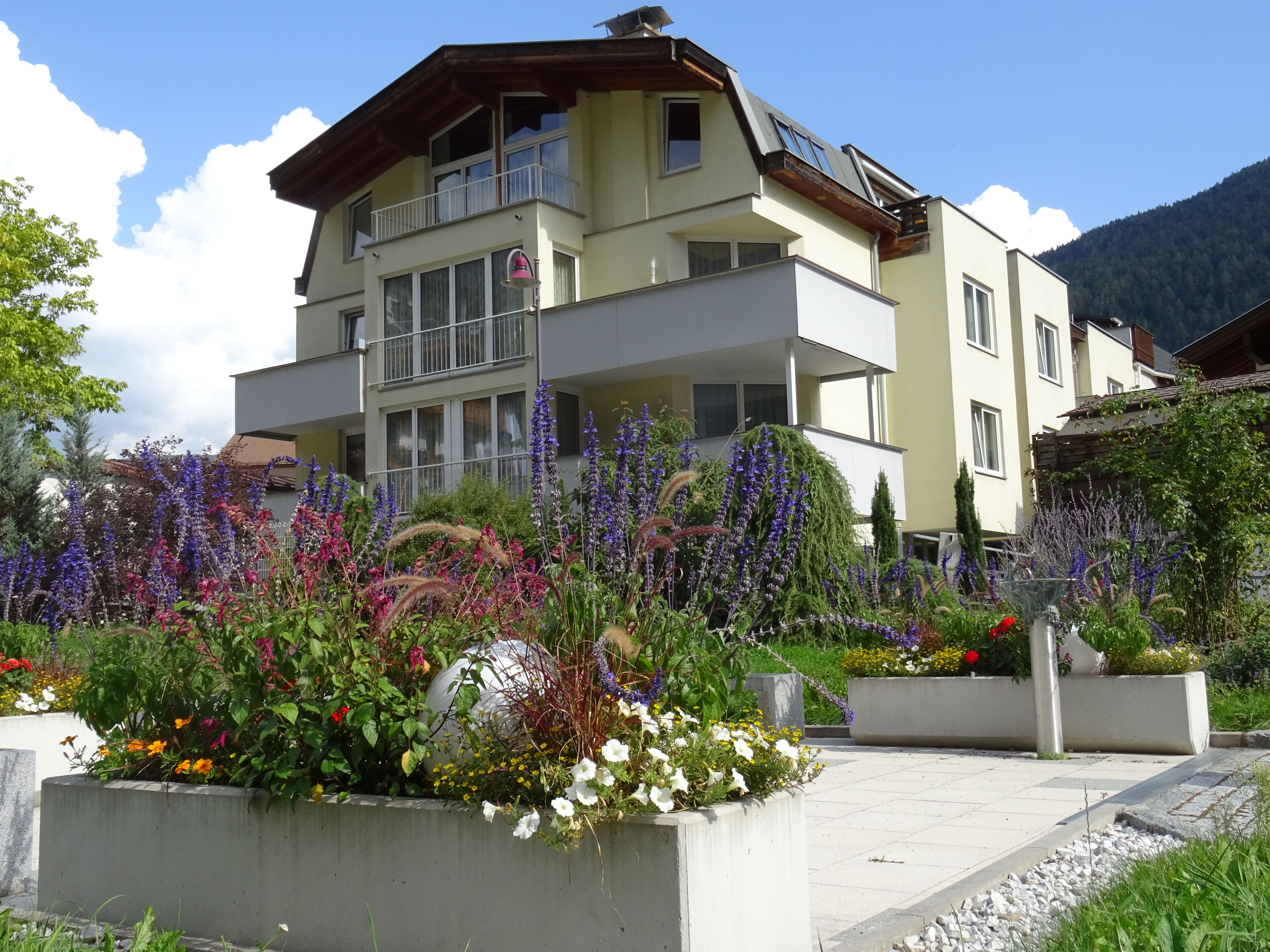 A multi-story building with balconies, surrounded by a variety of flowering plants and shrubs.