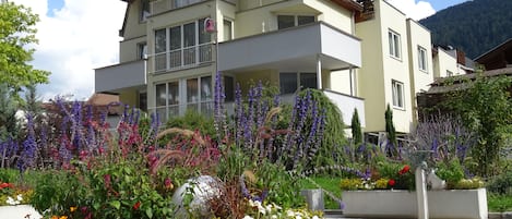 A multi-story building with balconies, surrounded by a variety of flowering plants and shrubs.