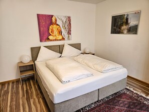 Un lit bien fait, avec du linge de lit blanc, une tête de lit et une table de chevet sur laquelle se trouve une lampe.