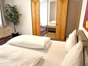 Ein Hotelzimmer mit einem Bett, einem Spiegel, einer Zimmerpflanze und einem Fenster mit Vorhängen.