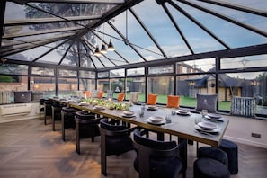 A conservatory with a dining table set for six, surrounded by chairs, and large windows offering views of the backyard. - Wind Farm (Lytham St. Anne's)