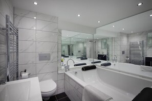 Een moderne badkamer met een grote spiegel, een badkuip, een toilet en een wastafel.