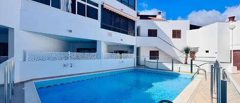A modern building with a swimming pool, balconies, and a clear blue sky.
