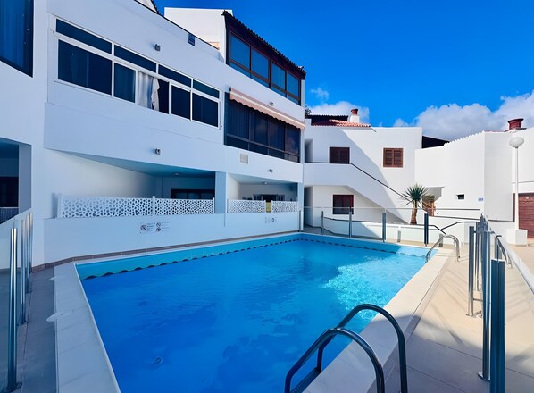 A modern building with a swimming pool, balconies, and a clear blue sky.