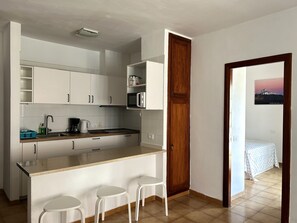 A compact kitchen with white cabinets, a microwave, and a coffee maker. There are three white stools at the counter. - Vacation Home 'Apt Colina 2, Los Cristianos K105' with Shared Pool, Private Terrace and Wi-Fi (Arona)