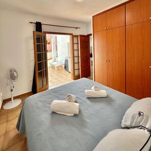 A bedroom with a bed, two pillows, a wooden wardrobe, a fan, and an open door leading to a balcony. - Vacation Home 'Apt Colina 2, Los Cristianos K105' with Shared Pool, Private Terrace and Wi-Fi (Arona)