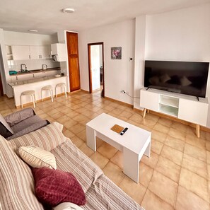 A modern living room with a sofa, a coffee table, and a TV. - Vacation Home 'Apt Colina 2, Los Cristianos K105' with Shared Pool, Private Terrace and Wi-Fi (Arona)