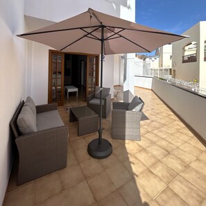 An outdoor patio with wicker furniture, a table, and a large umbrella.