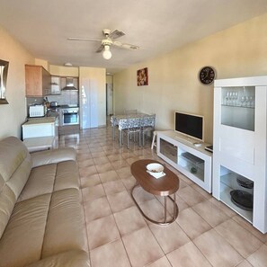 A living room with a sofa, a coffee table, a TV, a dining area with chairs, and a kitchen in the background. - Vacation Apartment 'Castle Harbor C118' with Sea View and Wi-Fi (Los Cristianos)