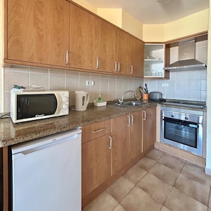 A kitchen with wooden cabinets, a microwave, a kettle, a sink, and an oven. - Vacation Apartment 'Castle Harbor C118' with Sea View and Wi-Fi (Los Cristianos)
