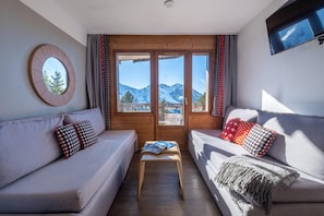 A cozy living room with a sofa and armchair, a small table, and a view of mountains through a large window. - 10m from ski slopes, balcony, ski locker, 20-22m², Avoriaz (Avoriaz)