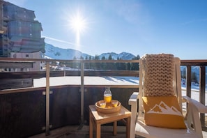 A balcony with a view of snow-covered mountains, a wooden chair with a cushion, and a table with a drink. - 10m from ski slopes, balcony, ski locker, 19-24m², Avoriaz (Avoriaz)
