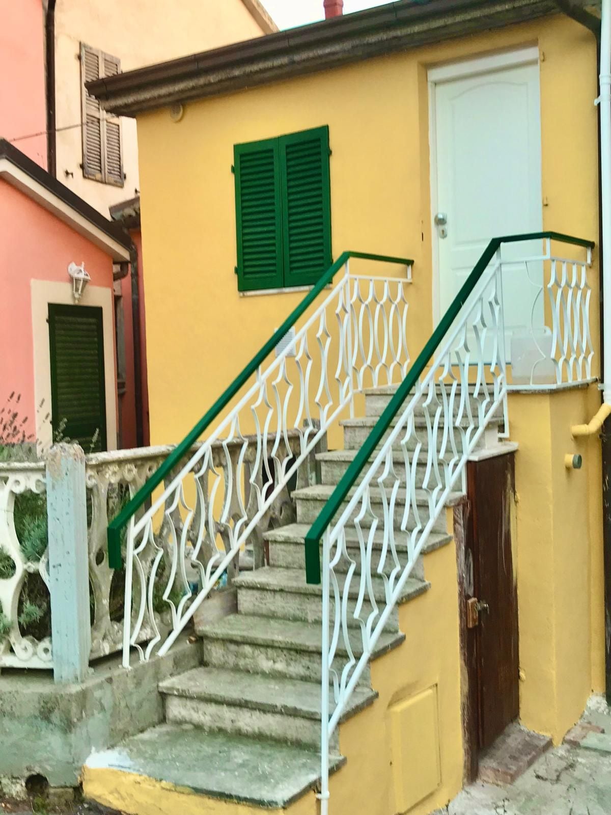 Eine Treppe mit weißen Geländern und grünen Akzenten, die zu einem gelben Gebäude mit einer weißen Tür und grünen Fensterläden führt.