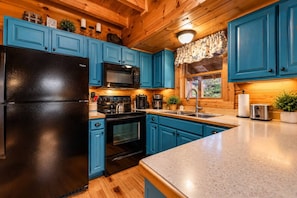 A kitchen with blue cabinets, a black refrigerator, a microwave, and a stove. - Blackberry Bliss | Hot Tub, Pool & Pet Friendly (Pigeon Forge)