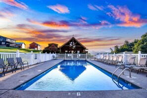 A swimming pool with lounge chairs and a wooden cabin in the background. - Blackberry Bliss | Hot Tub, Pool & Pet Friendly (Pigeon Forge)