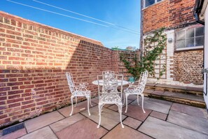 Un patio con pared de ladrillo, mesa y sillas de metal blanco, y pared de piedra con plantas trepadoras.