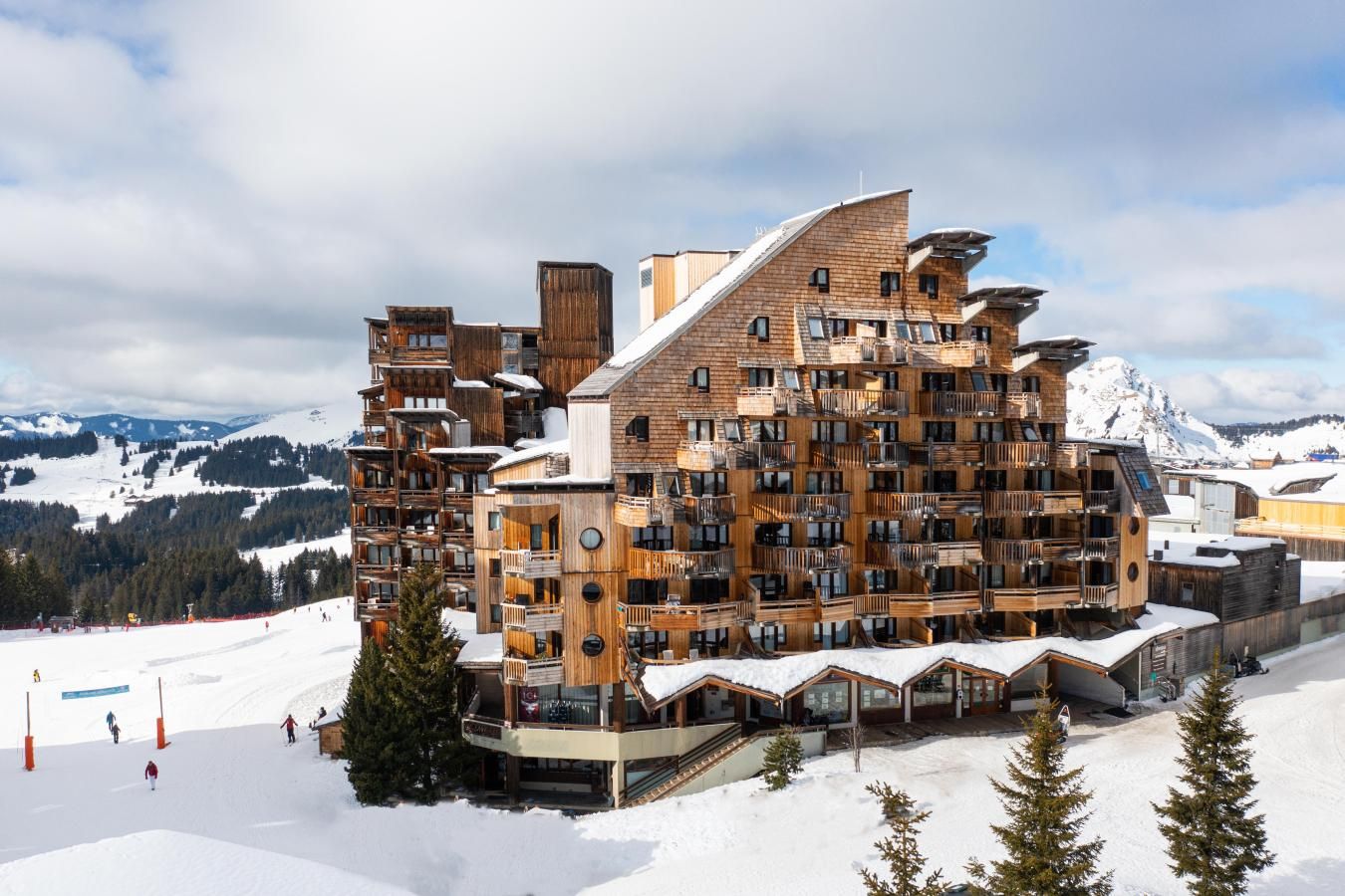 A multi-story wooden building with balconies, set against a snowy mountain backdrop.