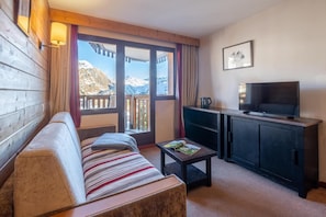 A room with a sofa, a small table, a television, and a cabinet. There is a window with a view of mountains. - 10m from ski slopes, balcony, ski locker, 25-35m², Avoriaz (Avoriaz)