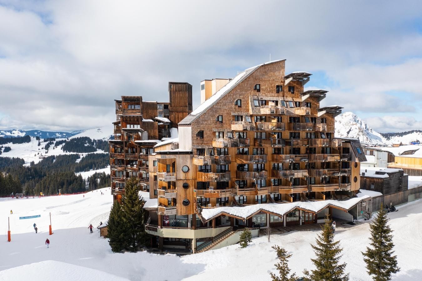 Un edificio de madera de varios pisos con balcones, frente a una imponente montaña nevada.