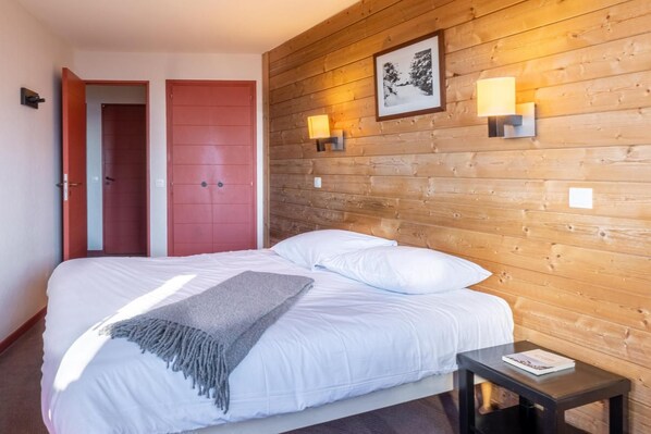 Ett hotellrum med en sänggavel i trä, en säng med vita sängkläder, en grå pläd, två sänglampor och en inramad tavla på väggen.