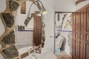 Ein Badezimmer mit einer Steinwand, einer Holztür, einem weißen Waschbecken und einem Spiegel.
