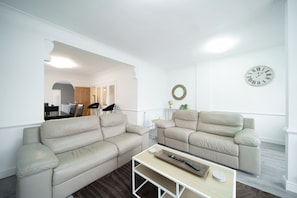 A modern living room with two beige sofas, a coffee table, and a wall clock. - Spacious Duplex Flat (Thornton-Cleveleys)