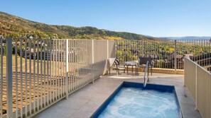 Zona de piscina al terrat amb vistes a un paisatge ondulat, una tanca blanca i mobiliari d'exterior.