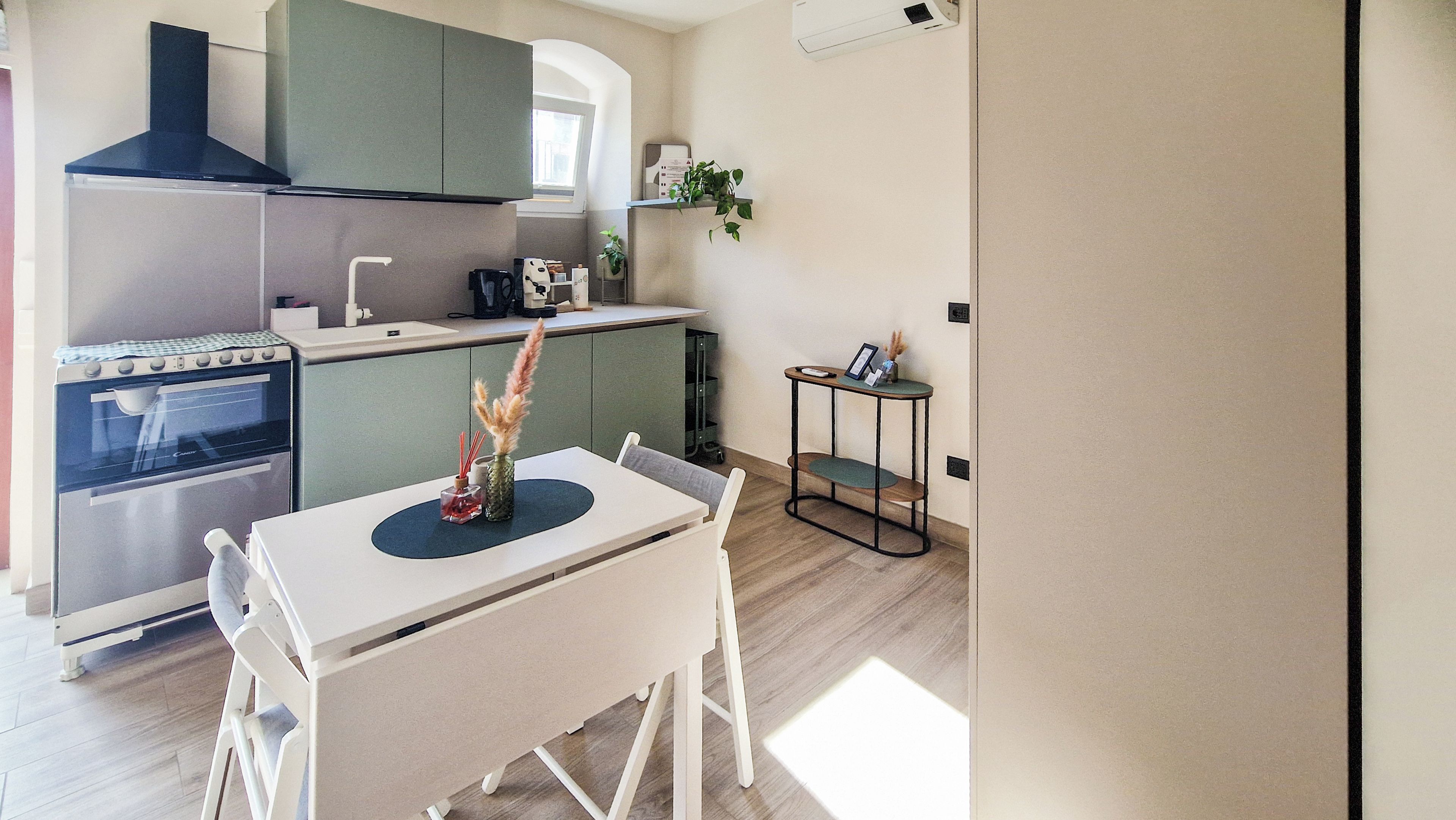 A modern kitchen with a built-in oven, a dining table with chairs, and a small side table with a plant.