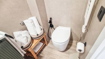 Une salle de bain comprenant des toilettes, un porte-serviettes, une étagère en bois avec des serviettes et un sèche-mains.