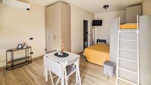 A compact bedroom with a bunk bed, a desk with a chair, a television, and a small table with a vase. - CB Apartments - Appartamento Cairoli (Bonito)