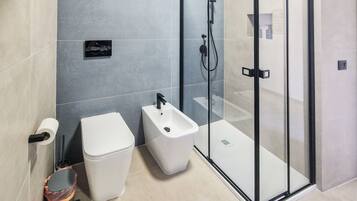 A modern bathroom with a toilet, bidet, and glass shower enclosure.
