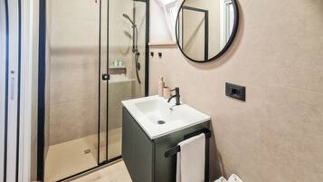 Une salle de bain moderne avec une douche à parois de verre, un lavabo blanc et un miroir rond.