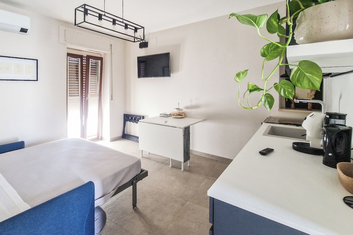 A small, well-lit room with a bed, a desk, a television, and a coffee maker.