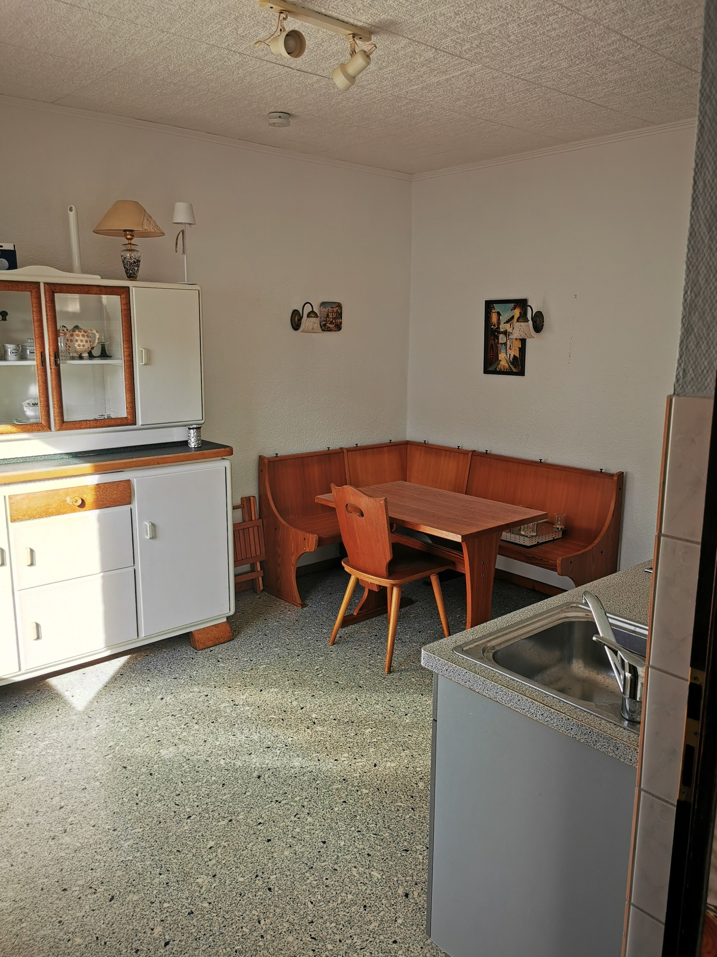 A compact kitchen with a wooden table, a bench, and a refrigerator.