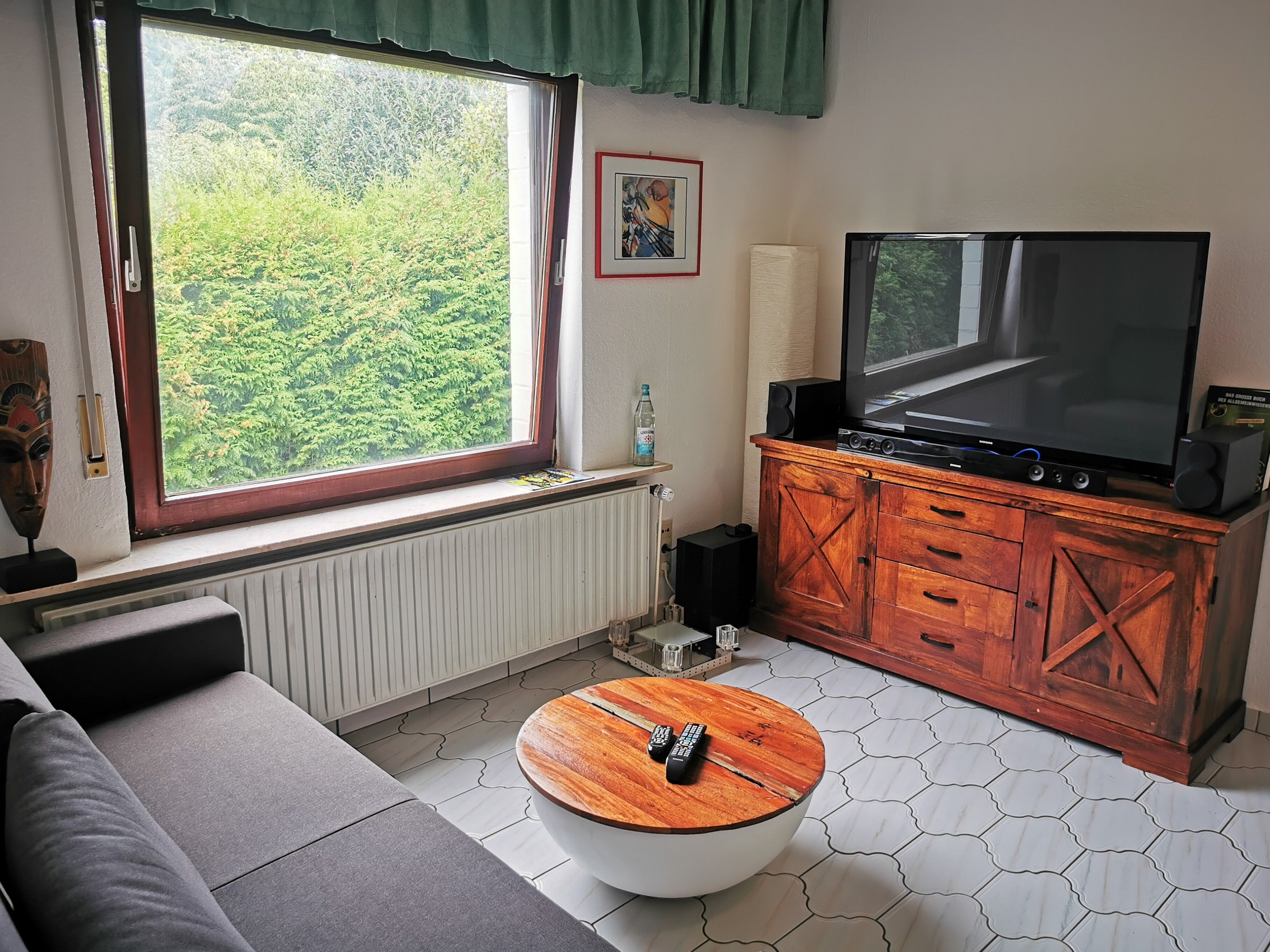 A living room with a large window, a flat-screen TV, a wooden cabinet, and a round coffee table.