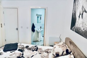 A bedroom with a bed, a door, a bathroom with a sink, and a wall-mounted artwork. - 2B/2B Haydock Flat M6 J23 A580 Gated Parking (Haydock)