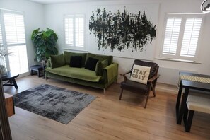 A living room with a green sofa, a chair with a pillow, a large plant, and a black abstract wall art piece. - 2B/2B Haydock Flat M6 J23 A580 Gated Parking (Haydock)