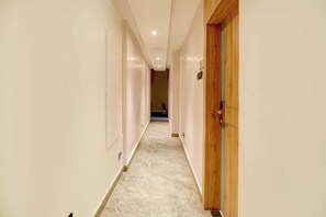 A hallway with a marble floor, wooden doors, and a number sign on the wall. - Palette Boragaon Formerly Midtown Inn (Guwahati)
