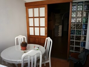 Ein Zimmer mit einem weißen runden Tisch, zwei weißen Stühlen, einer Topfpflanze und einer Holztür mit Glasfeldern.