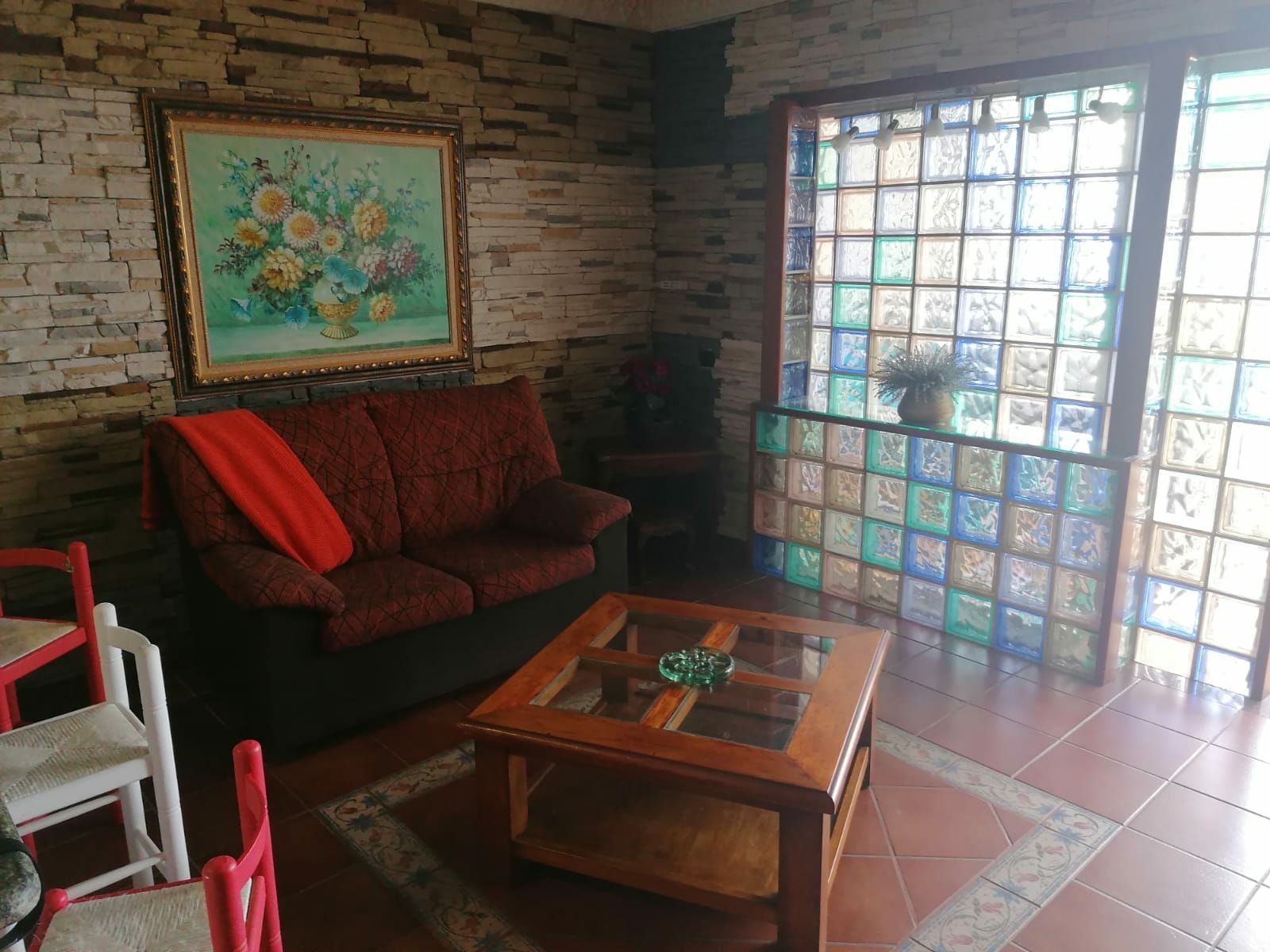 Una sala de estar con pared de ladrillo, sofá rojo, mesa de centro de madera y un ventanal con vidrios de colores.