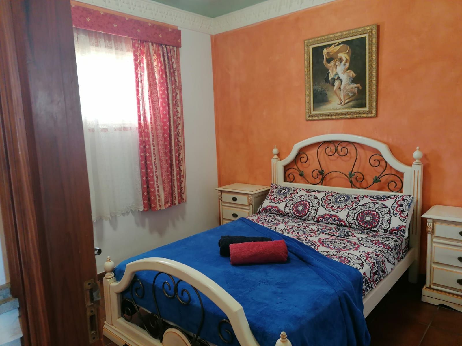 Un dormitorio con cama, mesita de noche, cómoda, ventana con cortinas y un cuadro en la pared.