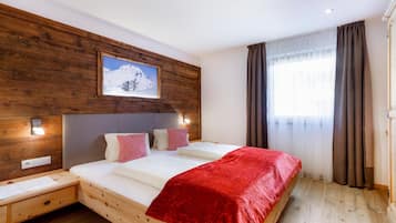 Una camera d'albergo con una testiera in legno, un letto grande con una coperta rossa, un comodino, una lampada a parete e una finestra con tende.