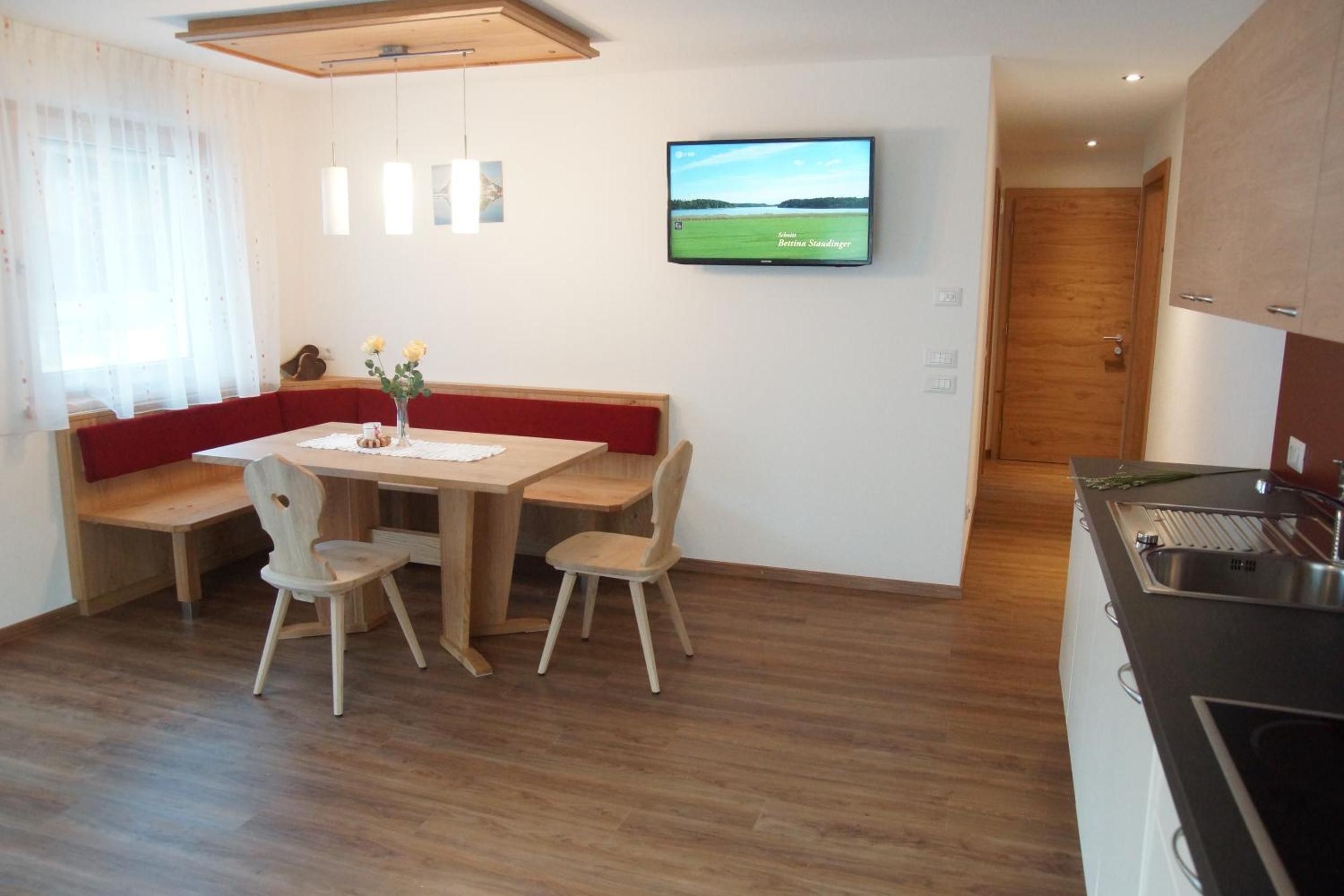 Ein Essbereich mit einem Holztisch, zwei Stühlen, einer Bank und einem Fernseher an der Wand.