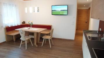 Ein Essbereich mit einem Holztisch, zwei Stühlen, einer Bank und einem Fernseher an der Wand.