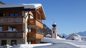 Una baita in legno con un balcone, una torre campanaria e montagne sullo sfondo.